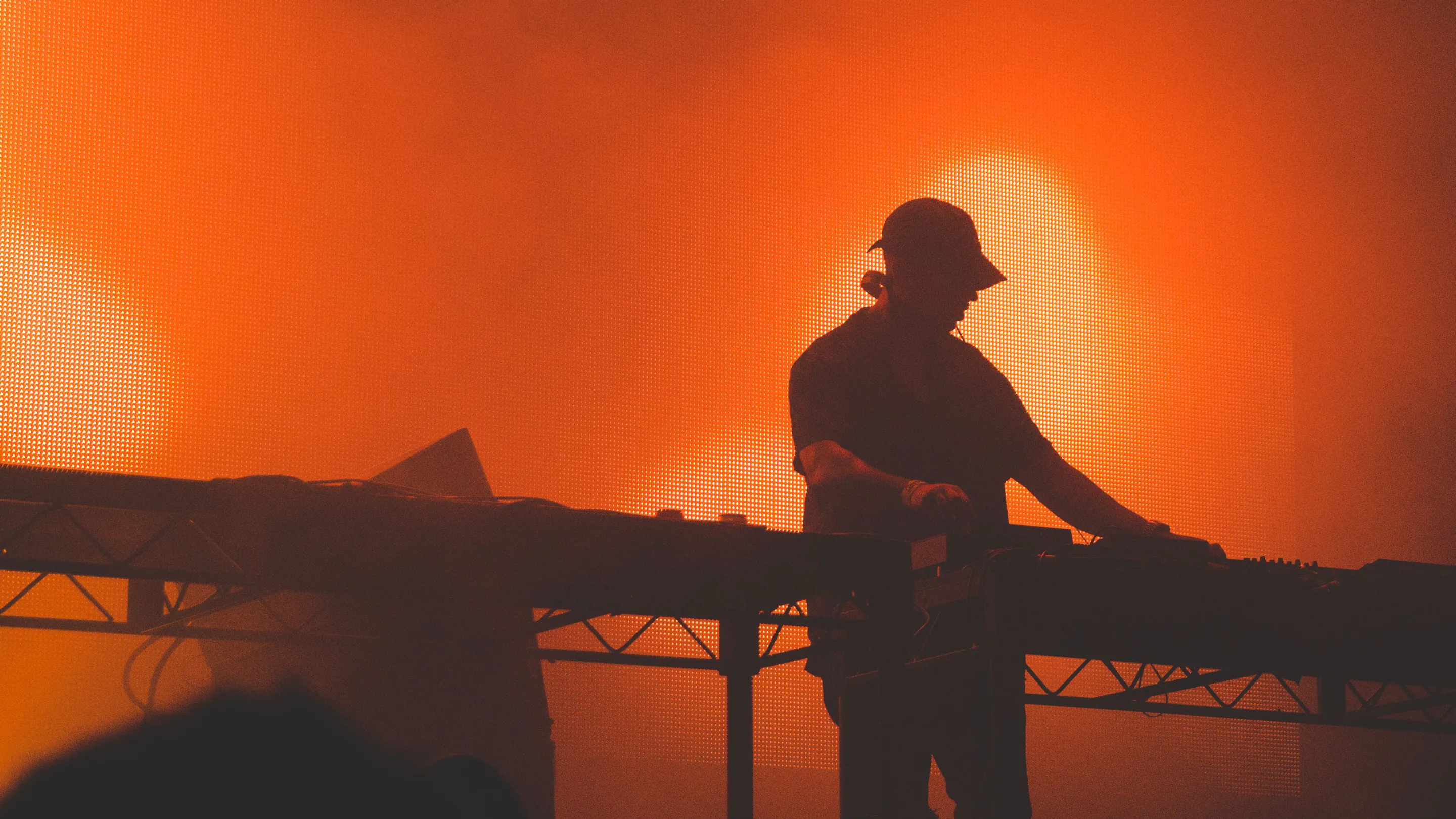 Ein DJ als Silhouette am Pult vor einer orange leuchtenden LED-Wand im Bühnennebel.